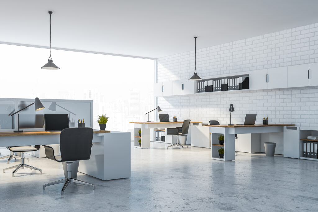 Interior of modern office with white brick walls, concrete floor, panoramic windows and long white and wooden computer tables. Cleared out and ready to clean and strip wax the floors.