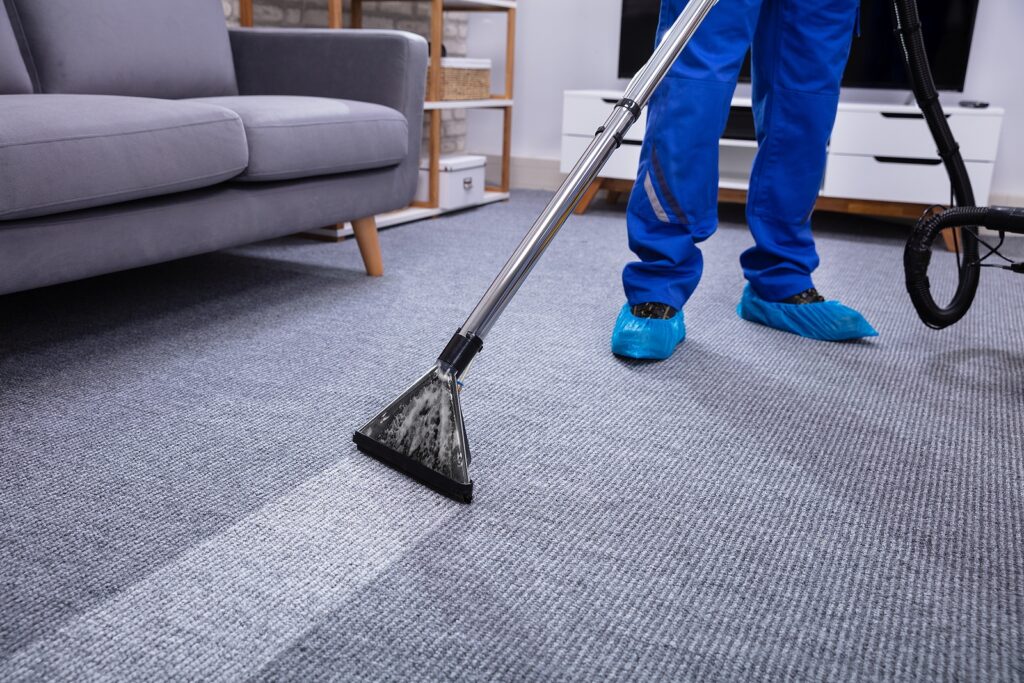 Low Section Of A Male Janitor Cleaning Carpet With Vacuum Cleaning In The Office or workspace