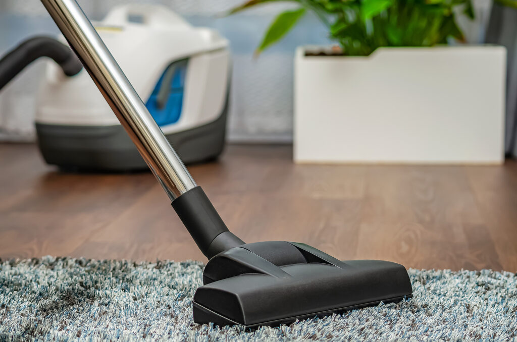 A person vacuums a gray carpet with a vacuum cleaner. Cleaning and cleanliness concept for workplaces and offices. 