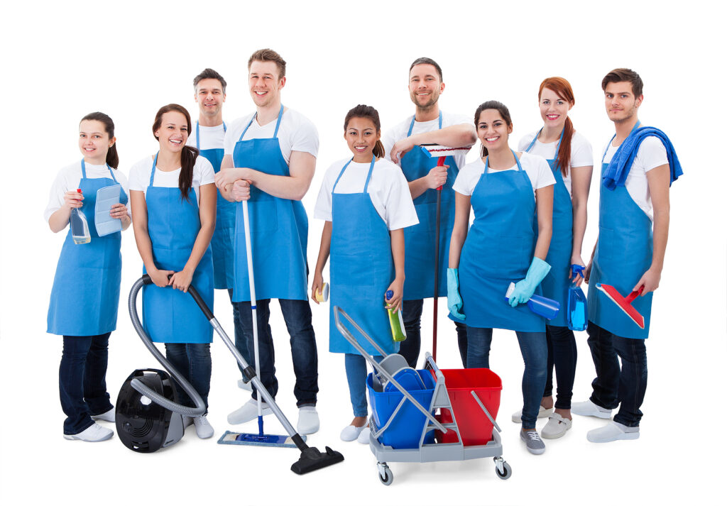 Large diverse group of janitors wearing blue aprons standing grouped together with their equipment smiling at the camera isolated on white background. Supplemental labor crew. 