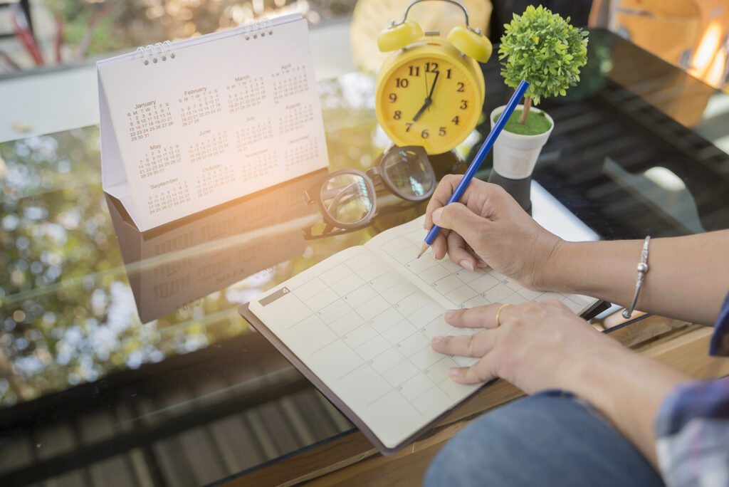 Woman hand planner or organizer writing on diary book and 2024 Calendar page.Female planning the year of business and staffing needed. 